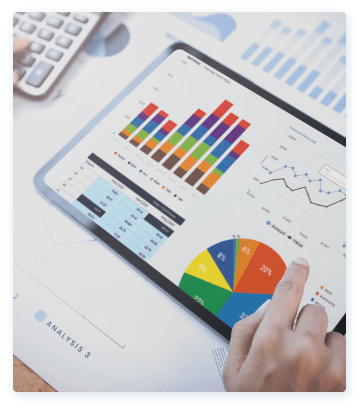 A tablet displaying various colorful business charts and graphs, including a bar chart, pie chart, and line graph. A hand is seen touching the tablet screen. A calculator and additional paper charts are partially visible in the background.