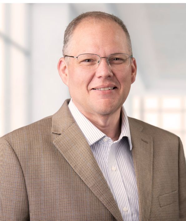 smiling man with glasses in a tan suit coat