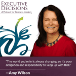 A woman with long dark hair, wearing a red top and a black necklace, smiles at the camera. A quote below reads, “The world you're in is always changing, so it's your obligation and responsibility to keep up with that." —Amy Wilson. Text on top reads "Executive Decisions: A Podcast for Business Leaders.