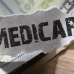 A close-up image of the word "Medicare" printed on a torn piece of paper positioned over a background that includes U.S. currency. It signifies financial aspects related to Medicare health insurance.