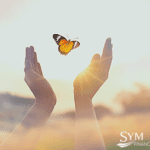 A pair of hands reaches towards a butterfly in flight, set against a serene, sunlit background. The butterfly, with its vibrant orange and black wings, symbolizes transformation. The logo for SYM Financial Advisors, an RIA firm dedicated to your financial growth, is in the bottom right corner.