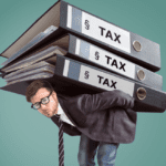 A man in a suit, glasses, and a striped tie bends under the heavy weight of three large binders labeled "TAX" stacked on his back. He appears strained as he balances the oversized folders, symbolizing the burden of estate tax mitigation, against a green background.